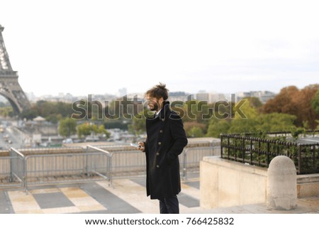 Handsome tourist using smartphone and enjoying France travel in slow motion.  Attractive guy dressed in black coat with earing and curly hair calling girlfriend. Concept of European trip an