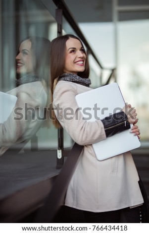 Happy woman with laptop waiting for someone outside office building
