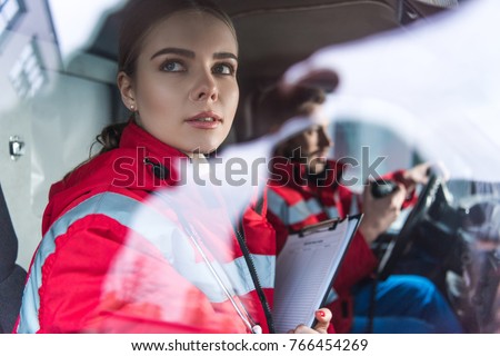 attractive young paramedic sitting in ambulance and looking away Royalty-Free Stock Photo #766454269