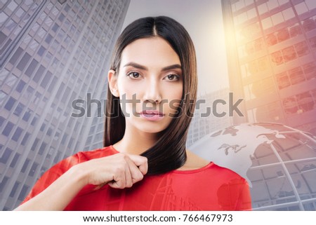 Very strong. Serious young woman checking the strength on her hair, touching it while standing against urban surroundings