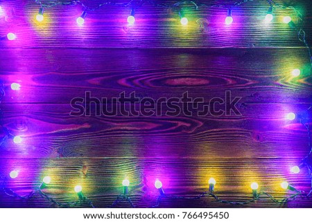 Wreath and garlands of colored light bulbs.Christmas background with lights and free text space. Christmas lights border. Glowing colorful Christmas lights on wooden background. New Year. 