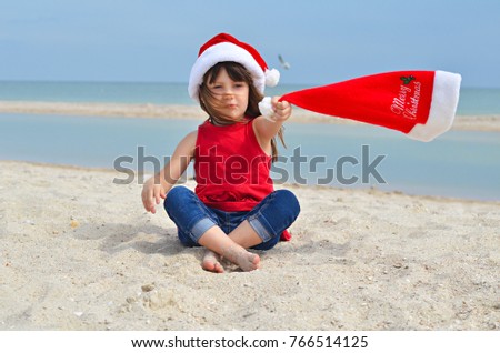 Cute little girl in Santa hat celebrating Christmas and New Year holidays on the beach