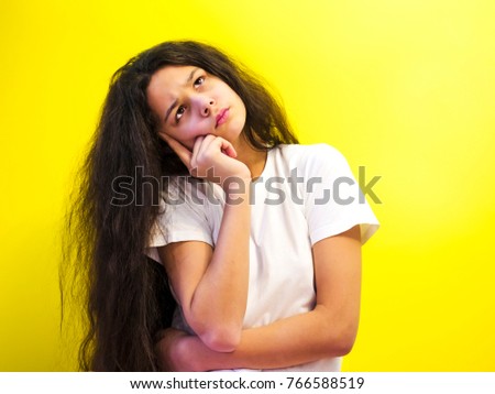 A thoughtful young woman touches her chin, thinks and looks up. Studio shot, isolated on yellow background