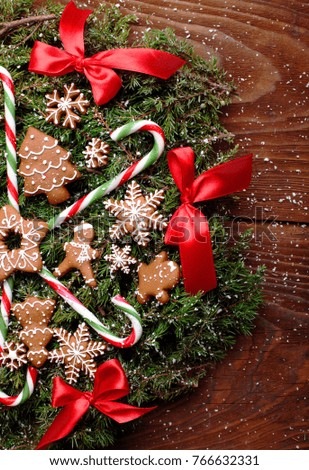 Christmas wreath of fir with ginger cookies,caramel sticks and red ribbon bows.On the wooden background.Snowy.Copy space