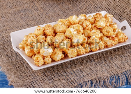 Popcorn with caramel on a white ceramic dish on sacking on a blue wooden background