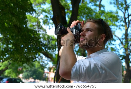 Photographer holds retro camera with big lense. Guy with serious face takes picture of cityscape. Man with beard holds photocamera on green park background. Photography concept.