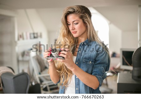 Indoor smiling lifestyle portrait of pretty young woman with camera