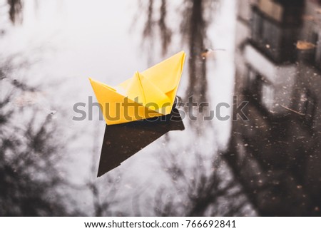 Yellow bright paper boat and autumn gloomy weather