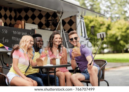 leisure, technology and people concept - happy young friends with food and drinks and taking selfie at food truck
