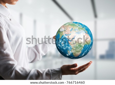 Side view closeup of business woman in shirt holding Earth globe in hands with office view on background. Elements of this image are furnished by NASA.