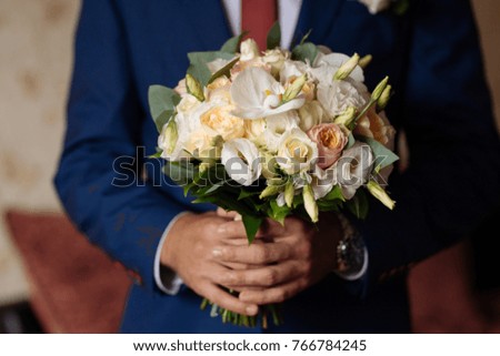 A big spring bouquet of the bride in the hands of the groom in a blue suit.