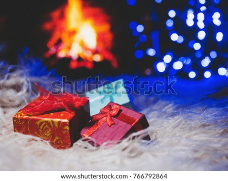 Christmas background with red and blue gift boxes on fur carpet in front of burning fireplace and Christmas tree. Empty place for text