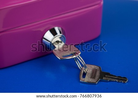 Pink metal box with lock and keys on a blue background.