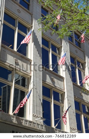 Low perspective on rows of American flags hanging below windows on the facade of an old fashion marble building, celebrating a United State holiday