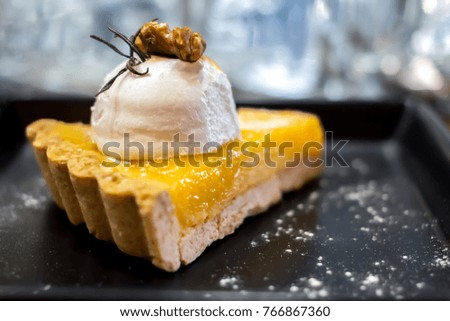 Lemon mousse pie with cream and nuts in black plate on wooden table background.