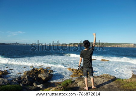 A success man put his hand up with camera in the other side sky sea view cheers 
