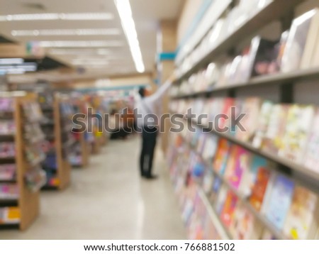Blurred image of man wearing white shirt stand in bookstore or bookshop and find a book at bookshelf with warm white lighting and bokeh background