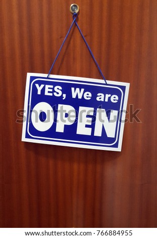 Brown flat door with a sign saying Yes We Are Open. Spanish building.