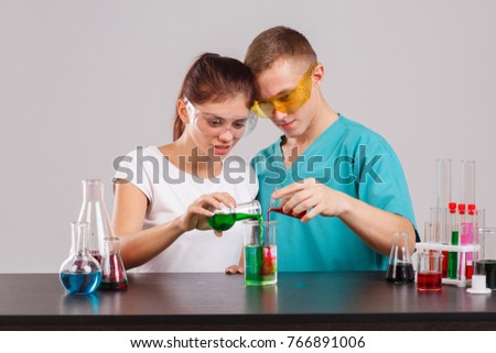 A pair assistant in uniform , poured a red and green liquid out of two small glass flasks into measuring cup.