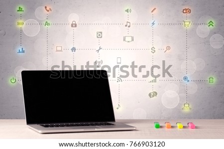 Notebook with blank screen sitting on office desk in front of background wall full of communication icons and illustrated connections concept