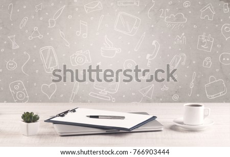 Close up of business office desk with laptop tablet in front of brown wall background full of drawn communication icons and school items concept