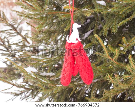 Red mittens with paper dog figure on fir tree green branches.