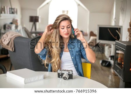 Indoor smiling lifestyle portrait of pretty young woman with camera spaks on the mobile phone