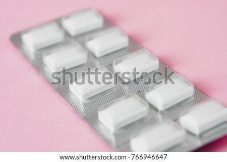 Close up of white chewable antacid pills or acid reducer tablets against heartburn and sour stomach in blister packaging on light pastel pink background