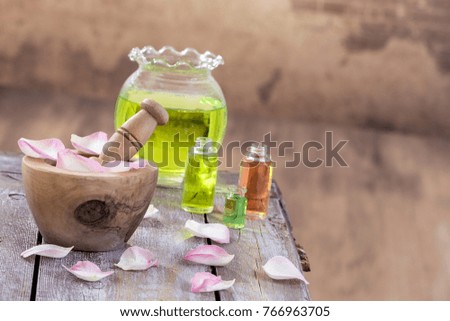 Spa and wellness concept: preparation of essential oil with pink roses, bottle of tincture and mortar on wooden board with all vintage wall