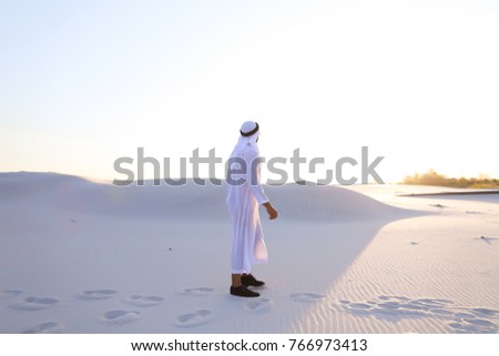 Handsome young Muslim driving along bottomless desert and looking toward sunset, admiring beauty of nature on warm clear night. attractive Muslim smiles widely and spreads hands to sides, straightens
