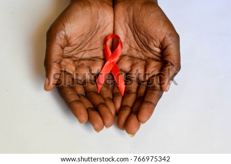 African dark brown skin cupped hands holding red ribbon for HIV AIDS Royalty-Free Stock Photo #766975342