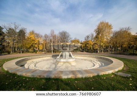 Empty water fountain in a park in an autumn sunny day with a blue sky and puffy clouds