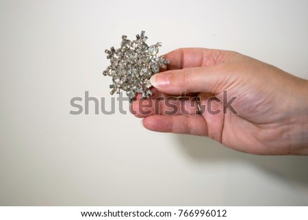 Fingers on extended hand displaying a star shaped broach in front of white background.