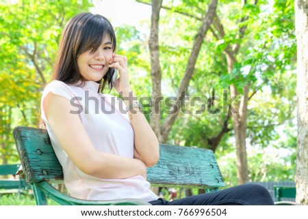Smiling beautiful women relaxing use cellphone in public park siting on bench