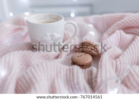 White cup with chocolate macaroons on pastel pink knit blanket.