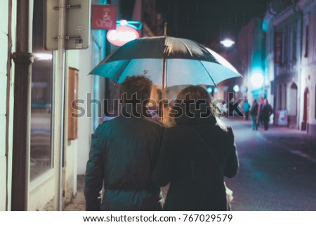 couple under an umbrella walking at the rain on a dark night road with rain eastern european