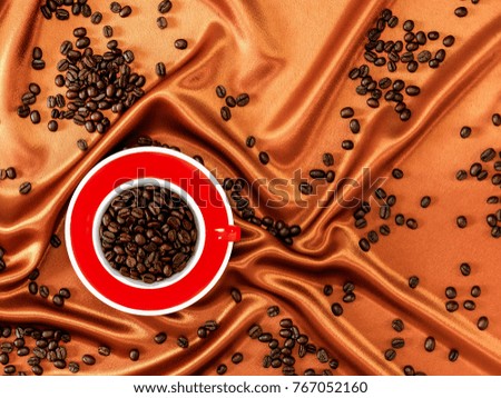 Flat lay of roasted coffee beans in a cup and some coffee beans scattered around on a fabric cover
