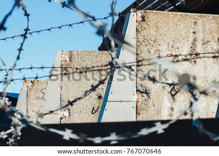 Barbed wire on top of the concrete fence with blue sky with clouds closeup