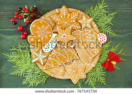 
Christmas gingerbread, decorative plate and ornaments lie on a wooden table of green color with twigs of a tree of thuja. Color photo.