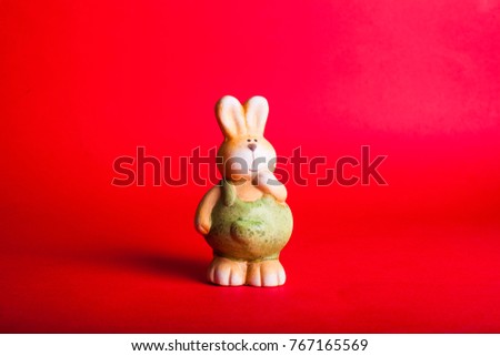 Little statue bunny with green grass near on  blur background photo of red wall