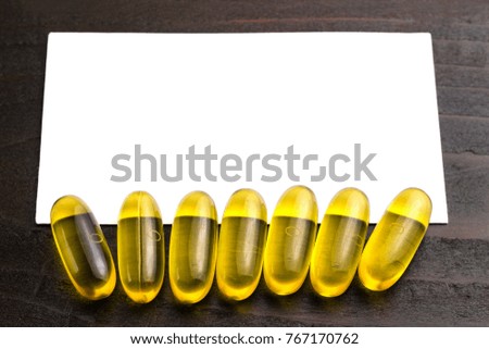 Yellow capsules omega 3, fatty acid, fish oil on dark wooden table with white card for your text, macro image.