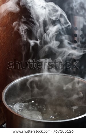 Steam rises above the boiling water in a metal pan Royalty-Free Stock Photo #767185126