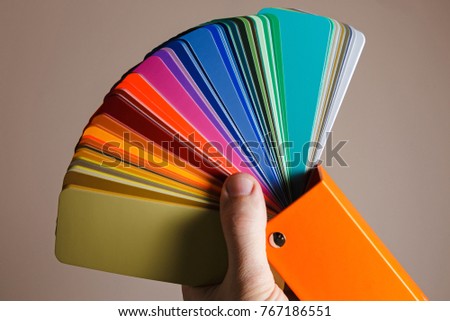 Sample colors catalogue for painting walls. Hand holding a color palette for repair.
