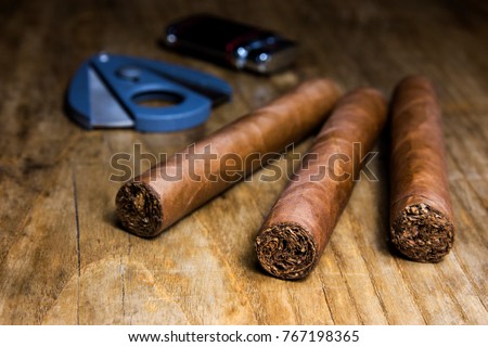 Three cigars with lighter and cutter on an old wooden table with blurred background Royalty-Free Stock Photo #767198365