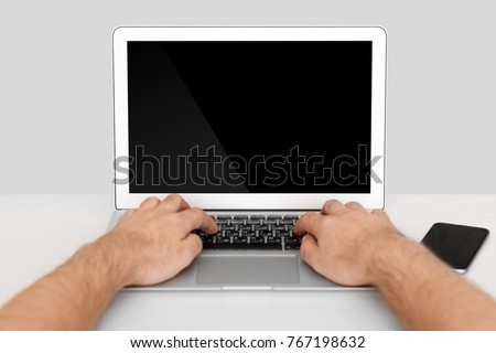Laptop on a white table, two hands on laptop a with a smartphone on an isolated background