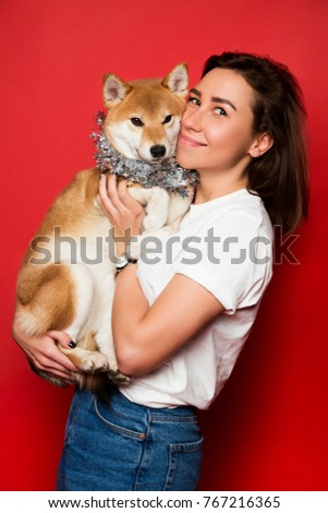 young brunette woman in white t shirt and jeans holding yellow white dog on her hands on plain red background
