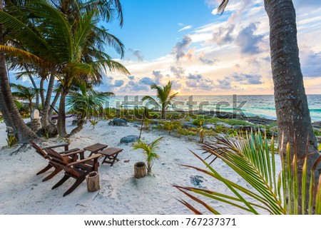 Sunset at paradise beach - Chairs under the palm trees on beach at tropical Resort. Riviera Maya - Caribbean coast at Tulum in Quintana Roo, Mexico Royalty-Free Stock Photo #767237371