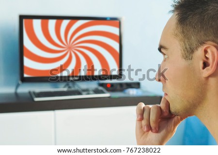 Brainwashed elderly man. hypnotic spiral on the screen of the TV. The young man hypnotized by false information on the monitor screen. False news on the Internet. viewer in front of the TV. Royalty-Free Stock Photo #767238022