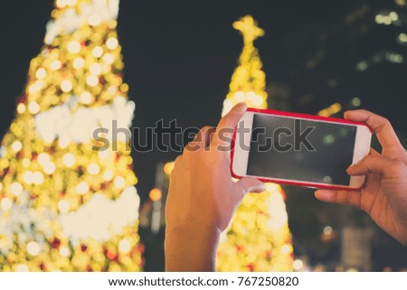 Hands taking picture of Christmas tree decoration. Girl holding smartphone on background glow bokeh Christmas illumination. mobile photography concept