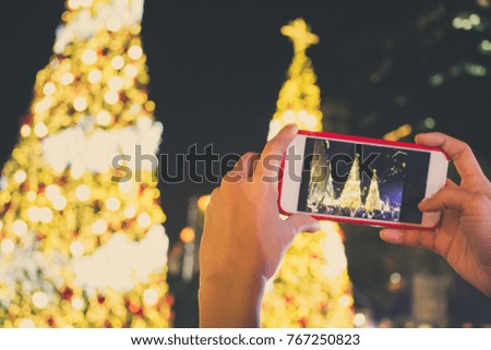 Hands taking picture of Christmas tree decoration. Girl holding smartphone on background glow bokeh Christmas illumination. mobile photography concept